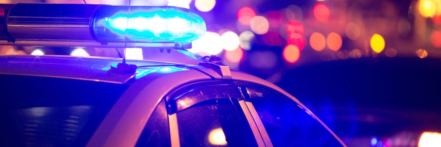 Blue light flasher atop of a police car. City lights on the back